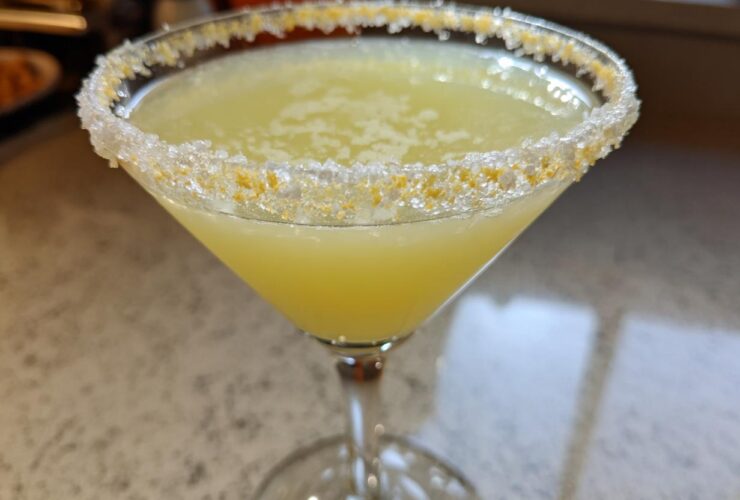 Close-up of a bright yellow lemon drop cocktail in a martini glass with a thick sugar and lemon zest rim.