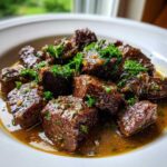 Close-up of tender, dark brown crockpot steak bites swimming in rich sauce and topped with fresh chopped parsley.
