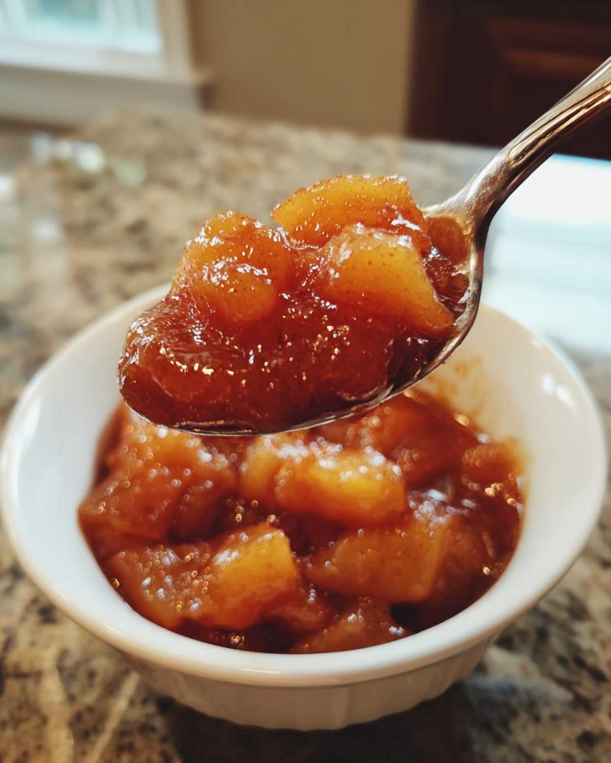 A spoonful of thick, glistening apple pie filling being lifted from a white bowl.