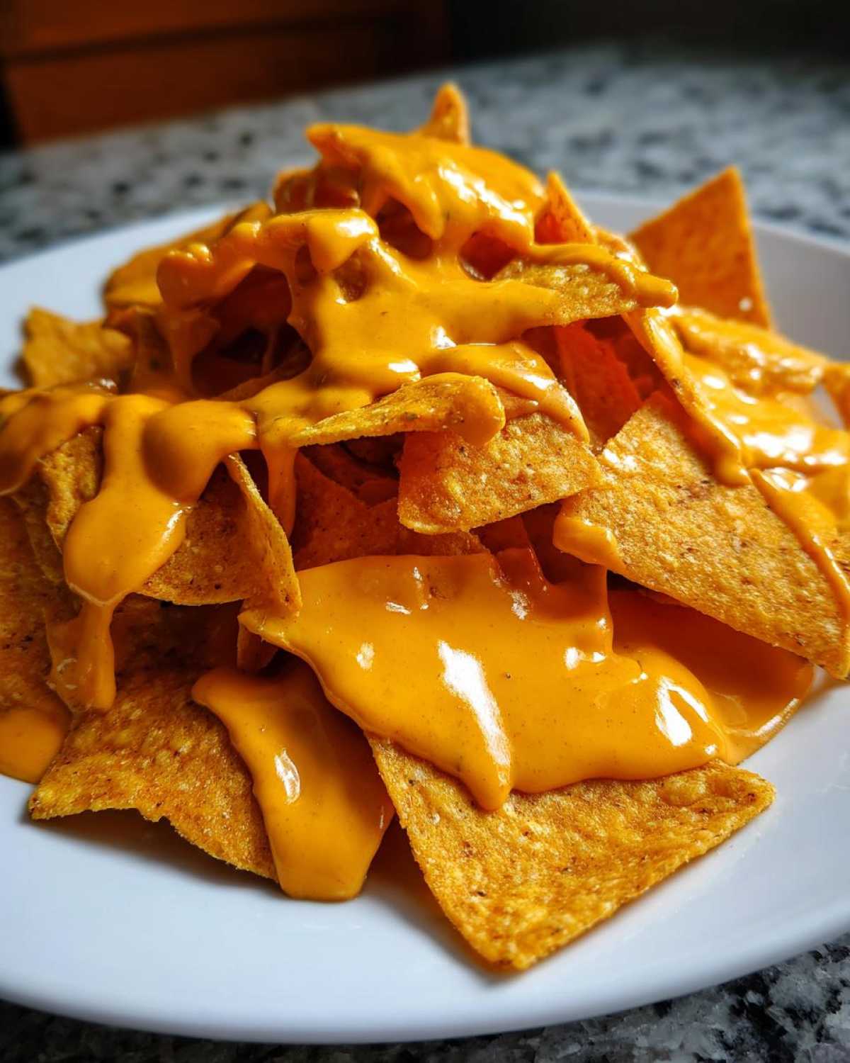 A close-up shot of tortilla chips piled high and generously covered in bright orange, creamy nacho cheese sauce.