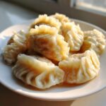 Close-up of several freshly steamed Traditional Chinese Dumplings piled on a white plate, catching warm sunlight.