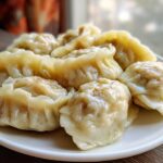 A close-up of several freshly steamed Traditional Chinese Dumplings arranged on a white plate.