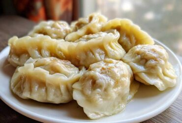 A close-up of several freshly steamed Traditional Chinese Dumplings arranged on a white plate.