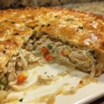 Close-up of a slice taken out of a golden-crusted turkey pot pie recipe, showing shredded turkey and mixed vegetables in creamy sauce.