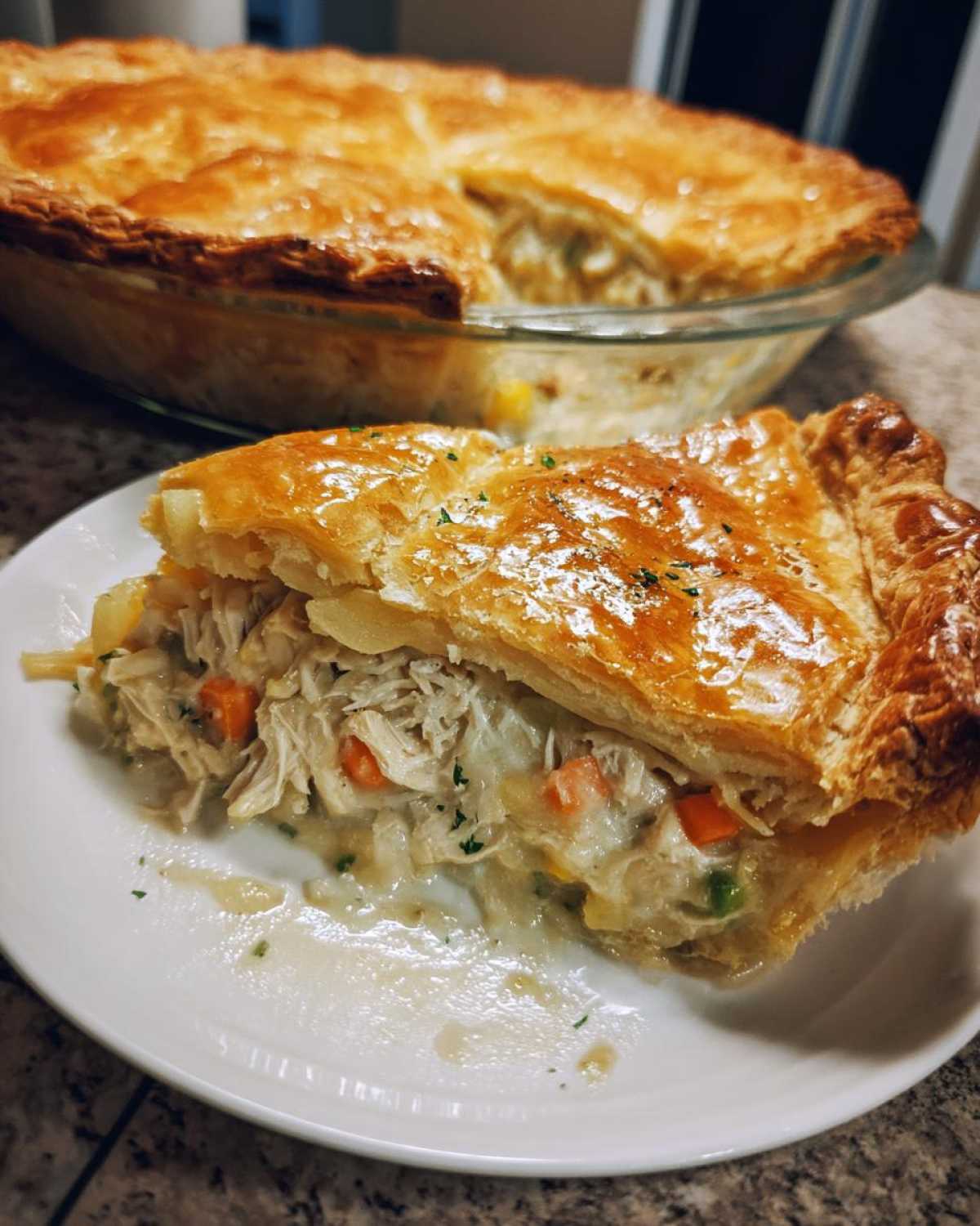 A close-up slice of flaky, golden brown turkey pot pie recipe on a white plate, showing shredded turkey and vegetables.