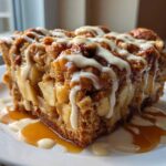 A close-up of a decadent slice of apple bread pudding topped with caramel and vanilla glaze.