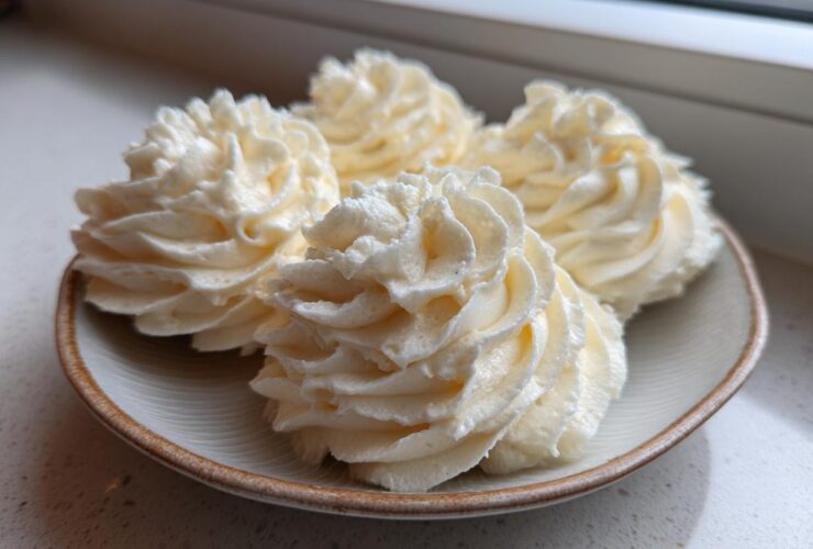 Four swirls of creamy, pale yellow vanilla buttercream frosting piped onto a small ceramic plate.