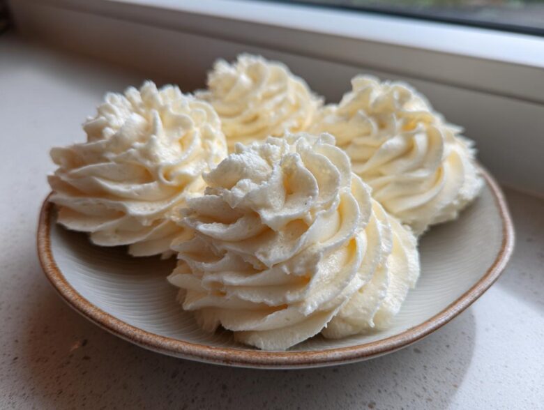 Four swirls of creamy, pale yellow vanilla buttercream frosting piped onto a small ceramic plate.
