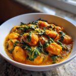Close-up of a white bowl filled with creamy vegan pumpkin curry mixed with wilted spinach.