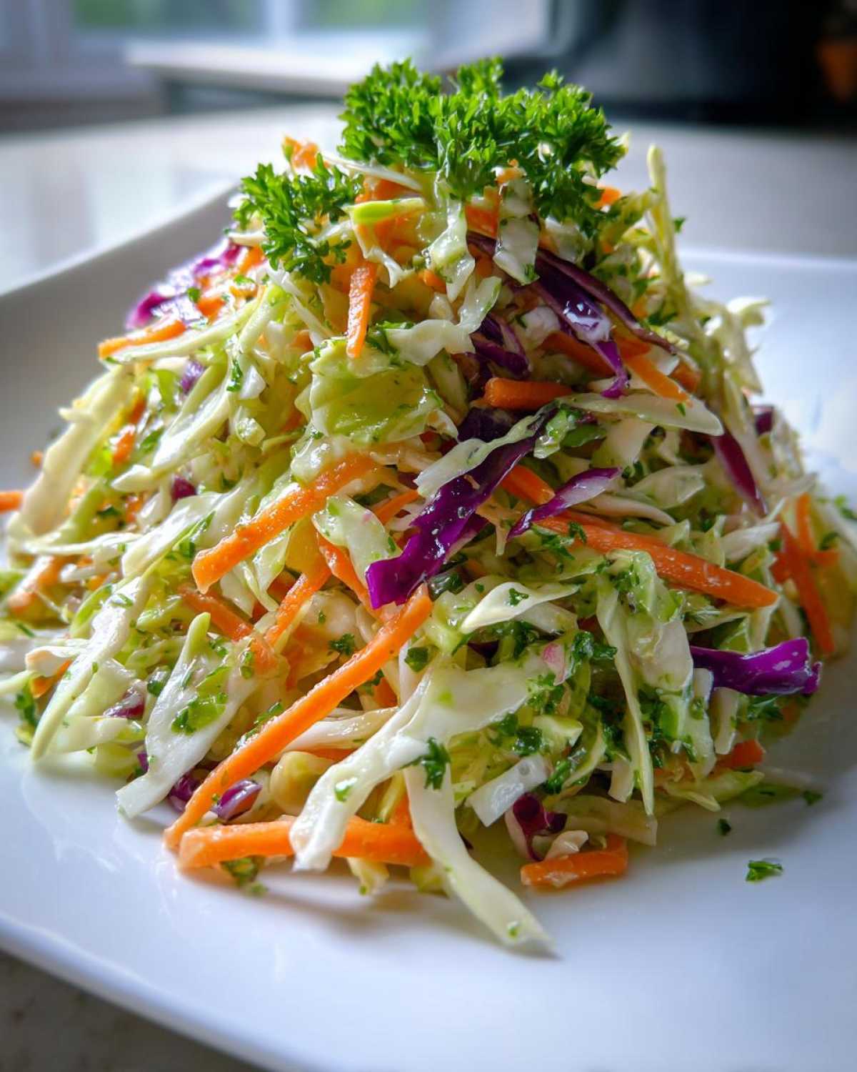 A mound of colorful, freshly dressed cabbage salad featuring shredded green and purple cabbage, bright orange carrots, topped with parsley.