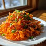 A vibrant mound of ribboned raw carrot salad topped with black sesame seeds and chopped green onions.