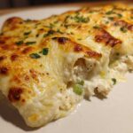 Close-up of creamy white chicken enchiladas topped with bubbly, browned melted cheese and parsley.