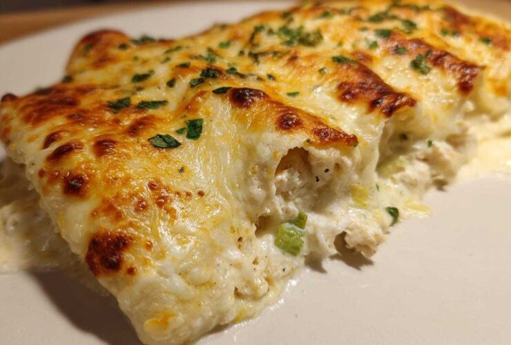 Close-up of creamy white chicken enchiladas topped with bubbly, browned melted cheese and parsley.