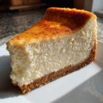 A thick, creamy slice of white chocolate cheesecake with a golden-brown top and graham cracker crust.