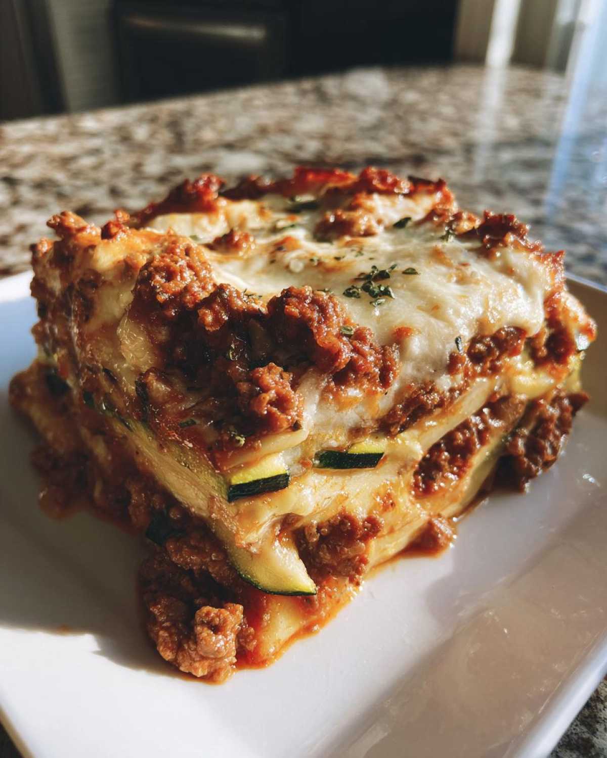 A thick slice of zucchini lasagna layered with meat sauce and melted cheese, showcasing zucchini noodles.