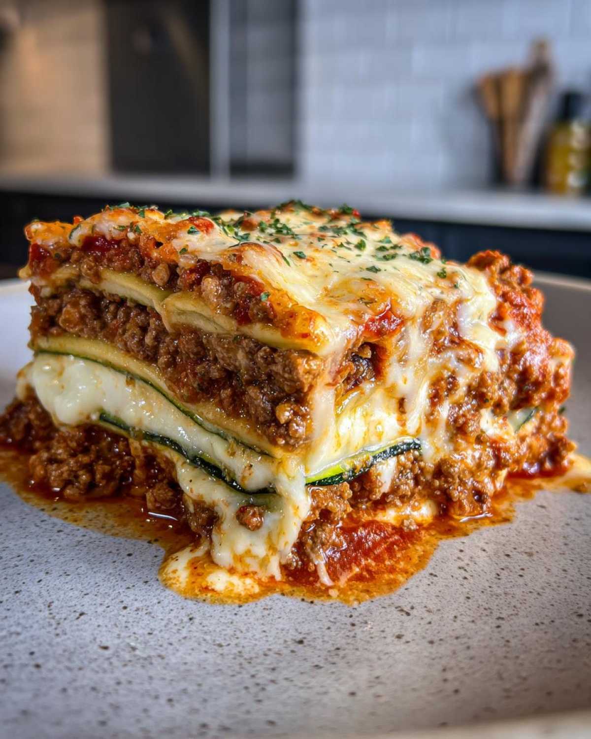 A thick, layered slice of zucchini lasagna featuring meat sauce and melted cheese, served on a speckled plate.
