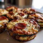 Close-up of several baked zucchini pizza bites topped with melted cheese and pepperoni slices.