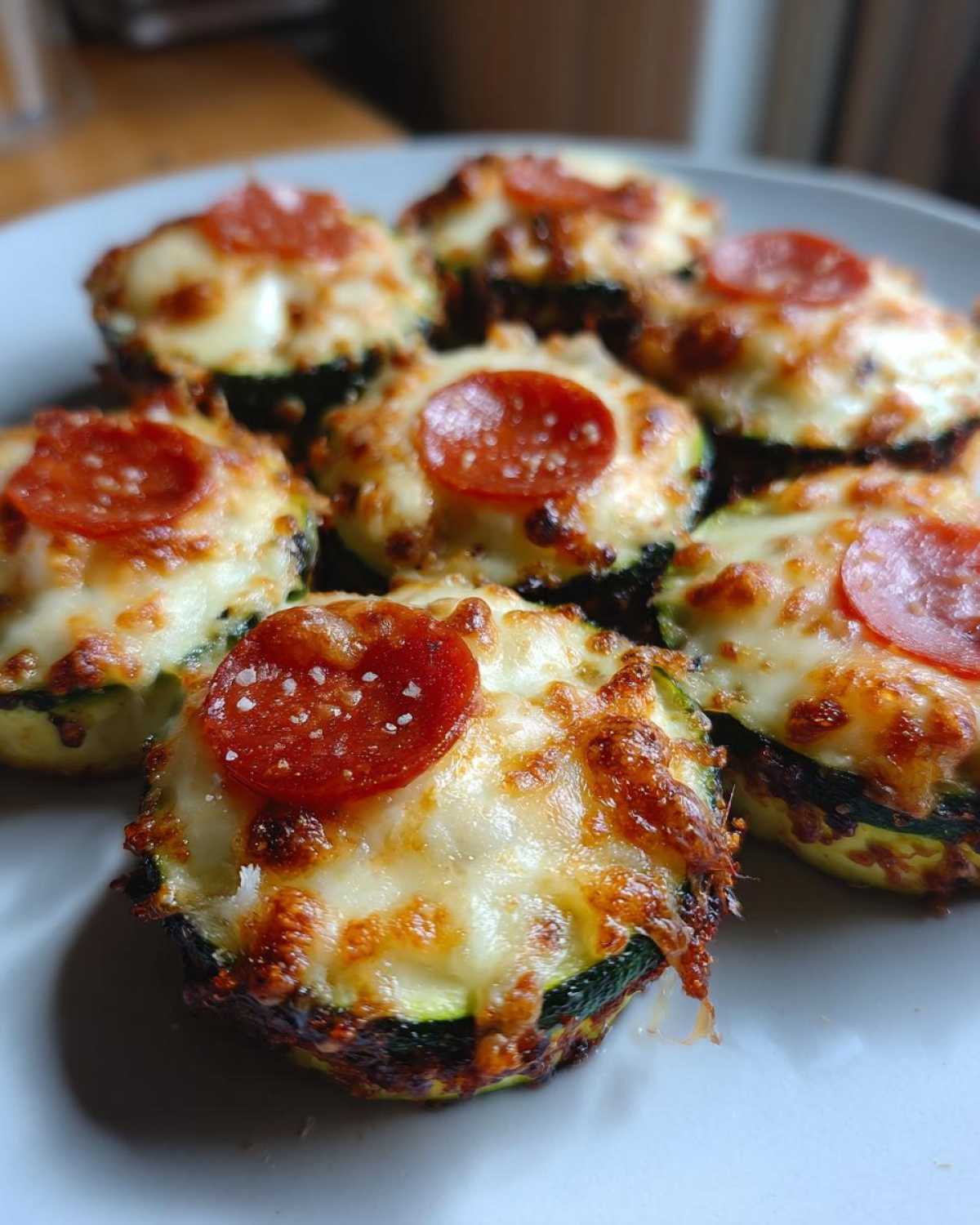 Close-up of baked zucchini pizza bites topped with melted cheese, pepperoni, and sea salt.
