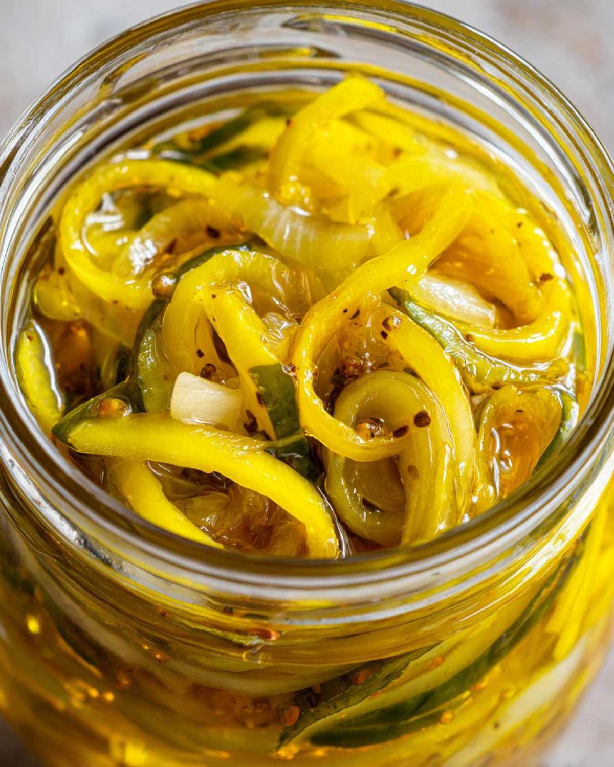 Close-up view inside a jar showing bright yellow, thinly sliced bread and butter pickle mixed with onions and spices.