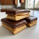 Three homemade buckeye graham crackers stacked, featuring a graham base, peanut butter filling, and a thick chocolate topping.