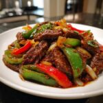 A close-up of savory Chinese pepper steak featuring tender beef strips mixed with bright green and red bell peppers and onions.