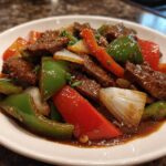 A close-up of vibrant Chinese pepper steak featuring tender beef strips, green and red bell peppers, and onions in a rich brown sauce.