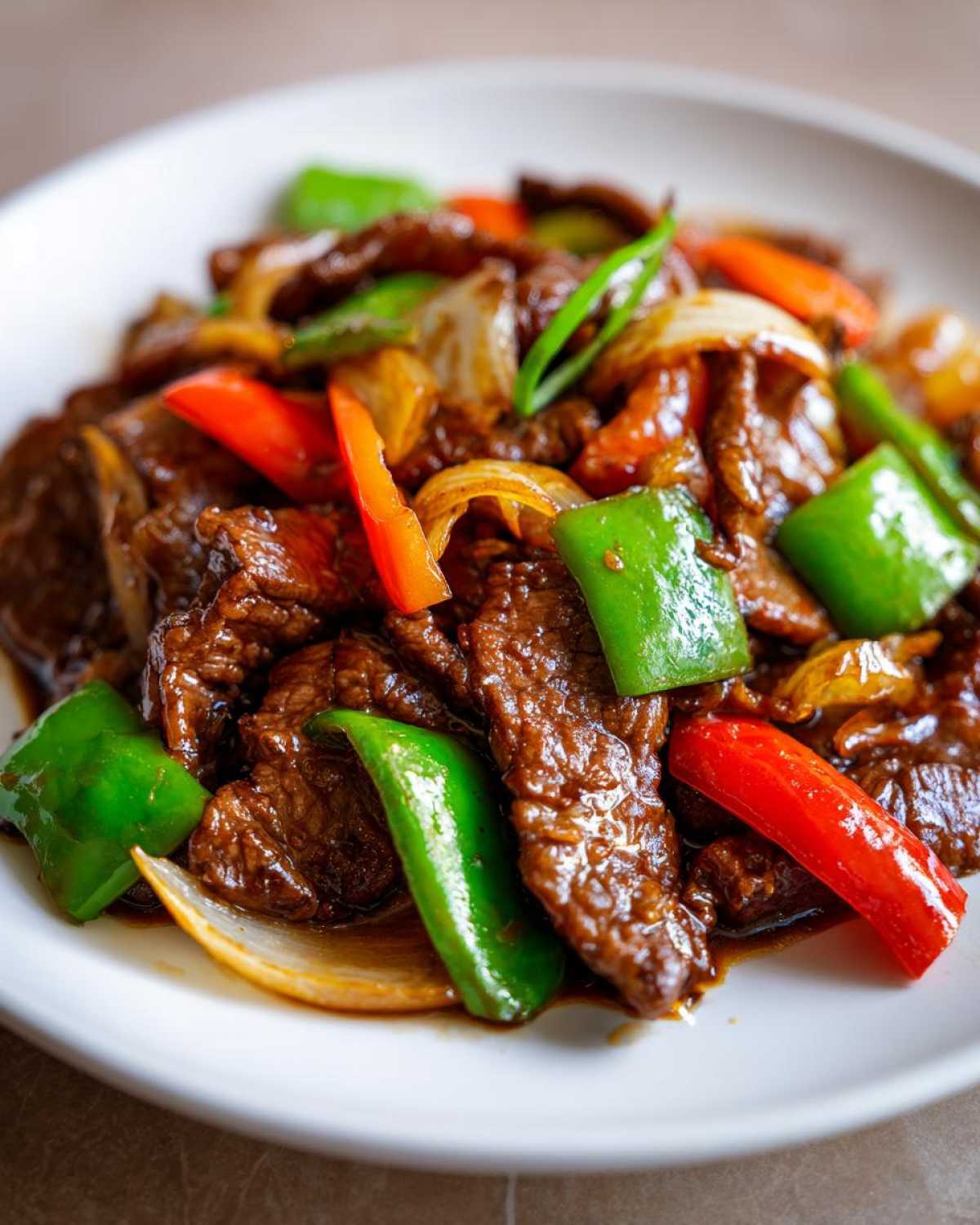 Close-up of glossy, saucy Chinese pepper steak mixed with bright green and red bell peppers and onions.