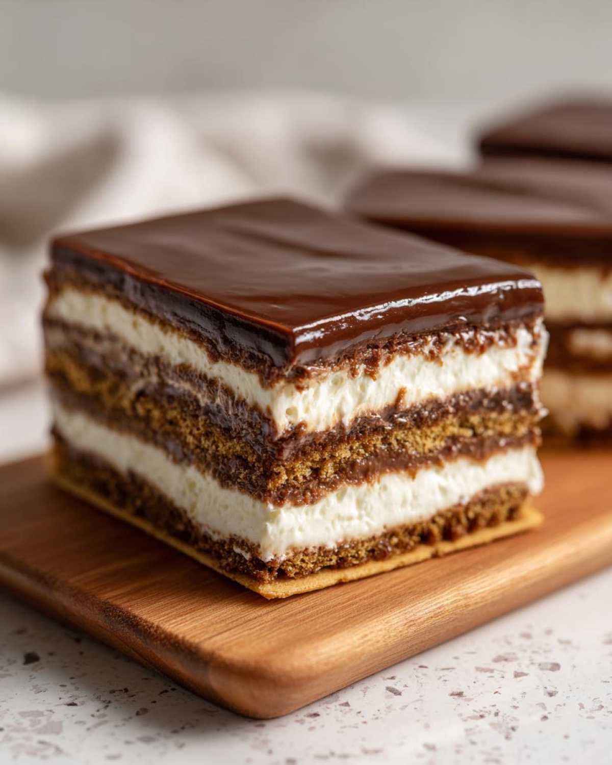 A perfect slice of chocolate eclair cake showing layers of graham cracker, cream filling, and chocolate ganache topping.