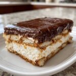 A delicious slice of chocolate eclair cake showing layers of creamy filling, graham crackers, and rich chocolate glaze.