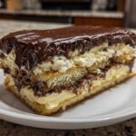A thick slice of chocolate eclair cake showing layers of pastry, vanilla cream, and rich chocolate frosting.