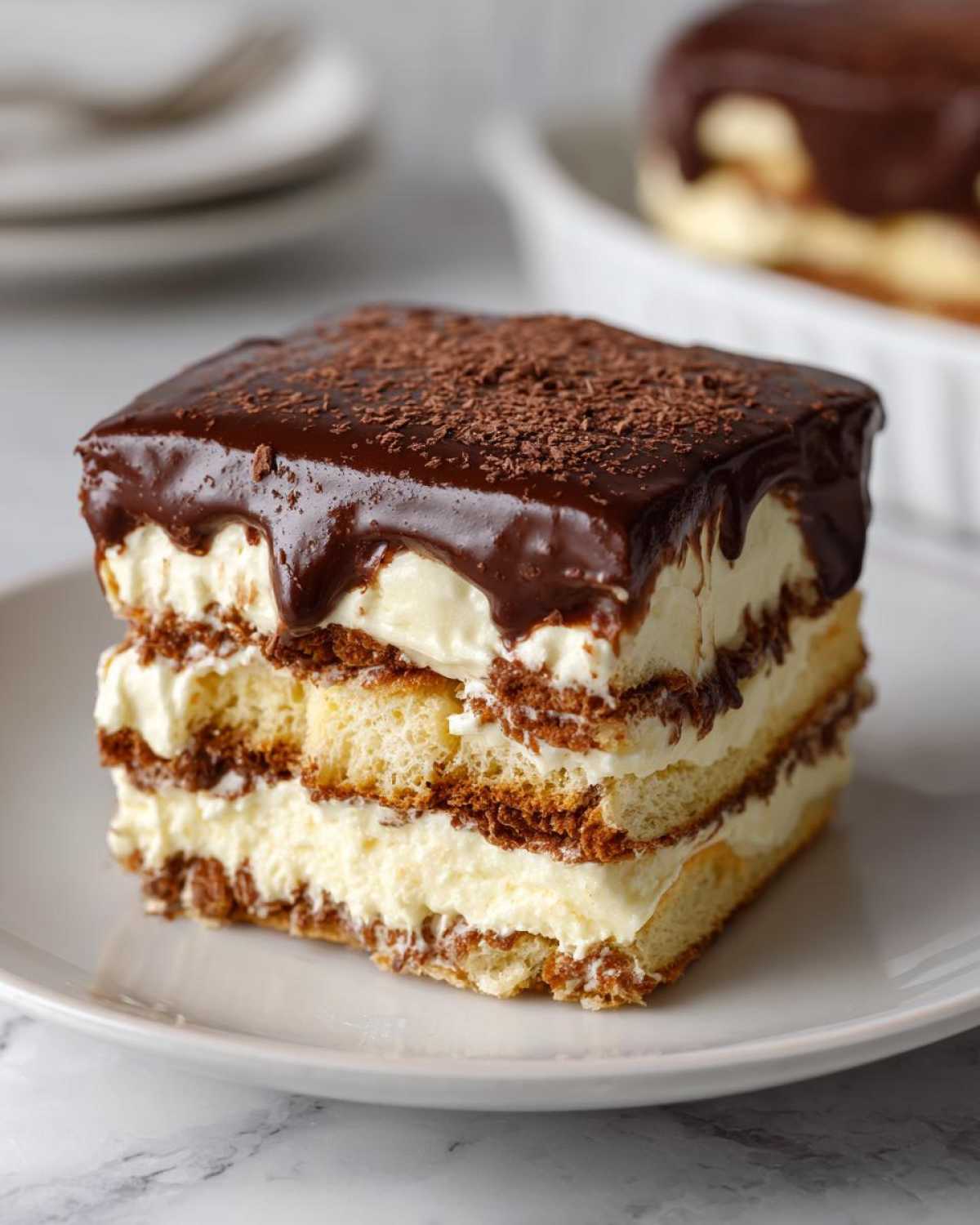 A perfect square slice of chocolate eclair cake showing layers of cake, cream filling, and rich chocolate ganache topping.