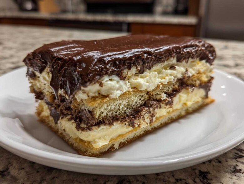 A thick slice of chocolate eclair cake showing layers of pastry, vanilla cream, and rich chocolate frosting.