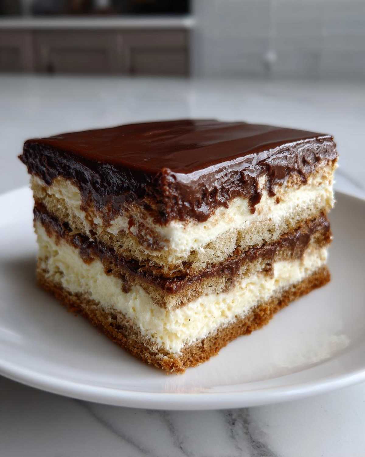 A square slice of chocolate eclair cake with layers of cake, cream, and chocolate ganache topping.