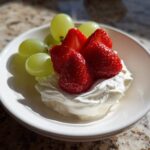 A serving of creamy fruit dip topped with fresh strawberries and green grapes.