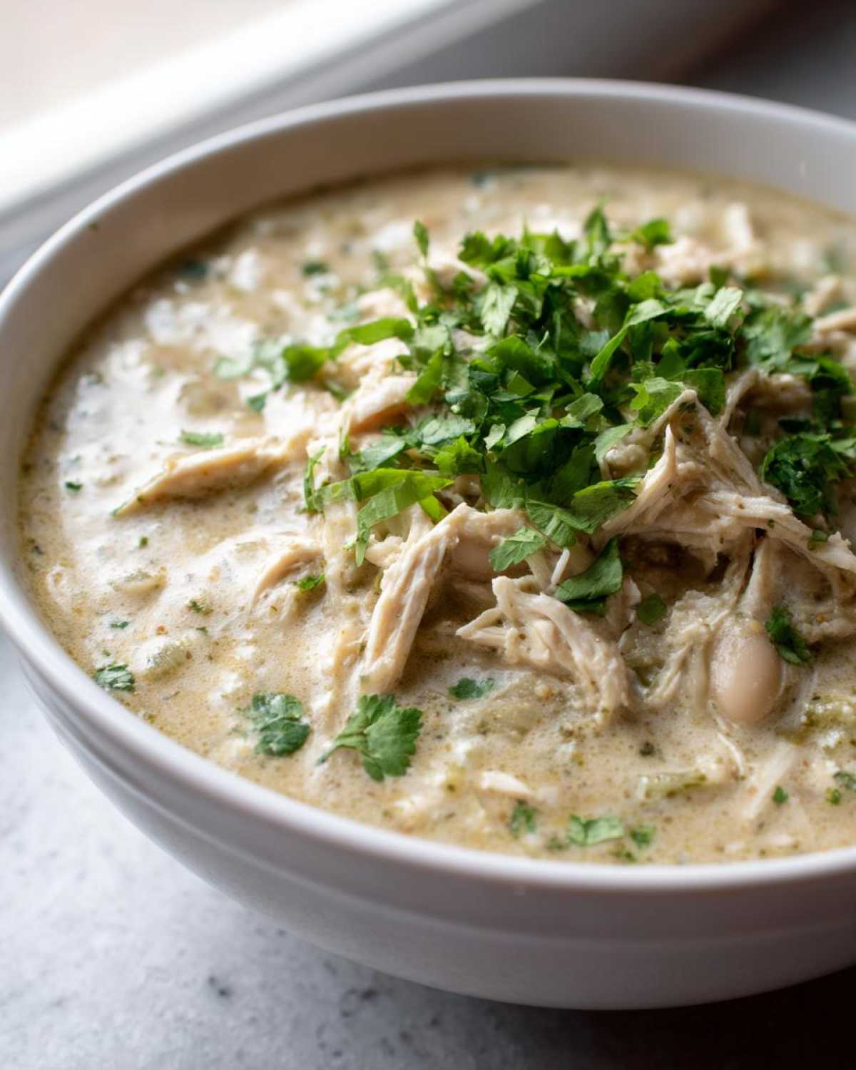 Close-up of creamy white chicken chili topped with shredded chicken and fresh cilantro.