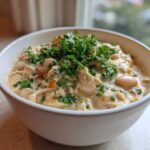 A close-up of a creamy white chicken chili topped generously with fresh chopped parsley in a white bowl.