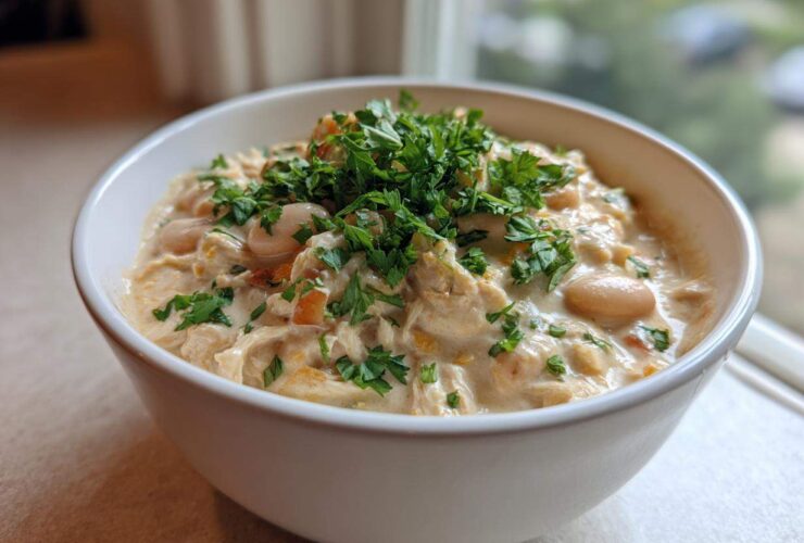 A close-up of a creamy white chicken chili topped generously with fresh chopped parsley in a white bowl.