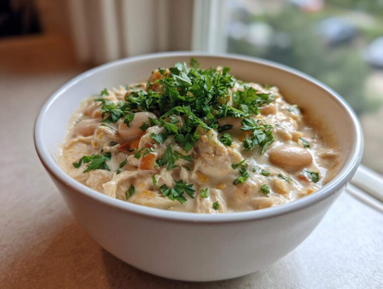 A close-up of a creamy white chicken chili topped generously with fresh chopped parsley in a white bowl.