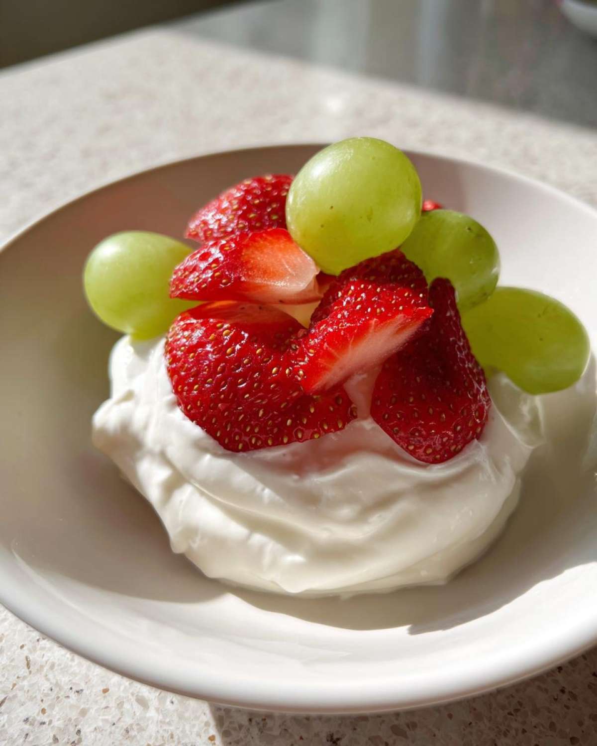 A serving of creamy fruit dip topped with fresh sliced strawberries and green grapes.