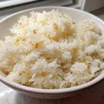 Close-up of a white bowl filled with fluffy, white garlic butter rice, showing golden bits of toasted garlic.