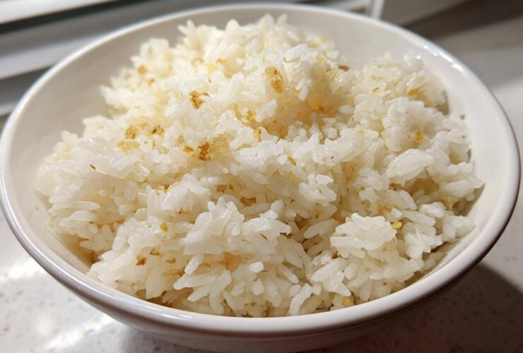Close-up of a white bowl filled with fluffy, white garlic butter rice, showing golden bits of toasted garlic.