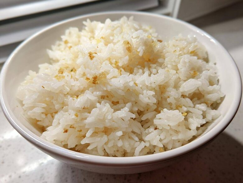 Close-up of a white bowl filled with fluffy, white garlic butter rice, showing golden bits of toasted garlic.