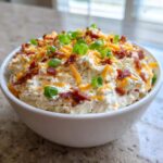 A bowl filled with creamy bacon cheddar cream cheese dip, topped with shredded cheese, bacon bits, and green onions.