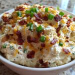 A close-up of a thick, creamy bacon cheddar cream cheese dip topped with crumbled bacon and fresh green onions.