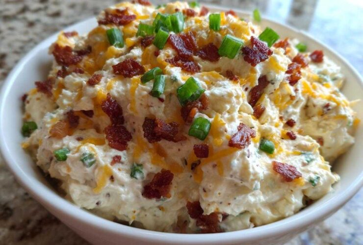 A close-up of a thick, creamy bacon cheddar cream cheese dip topped with crumbled bacon and fresh green onions.