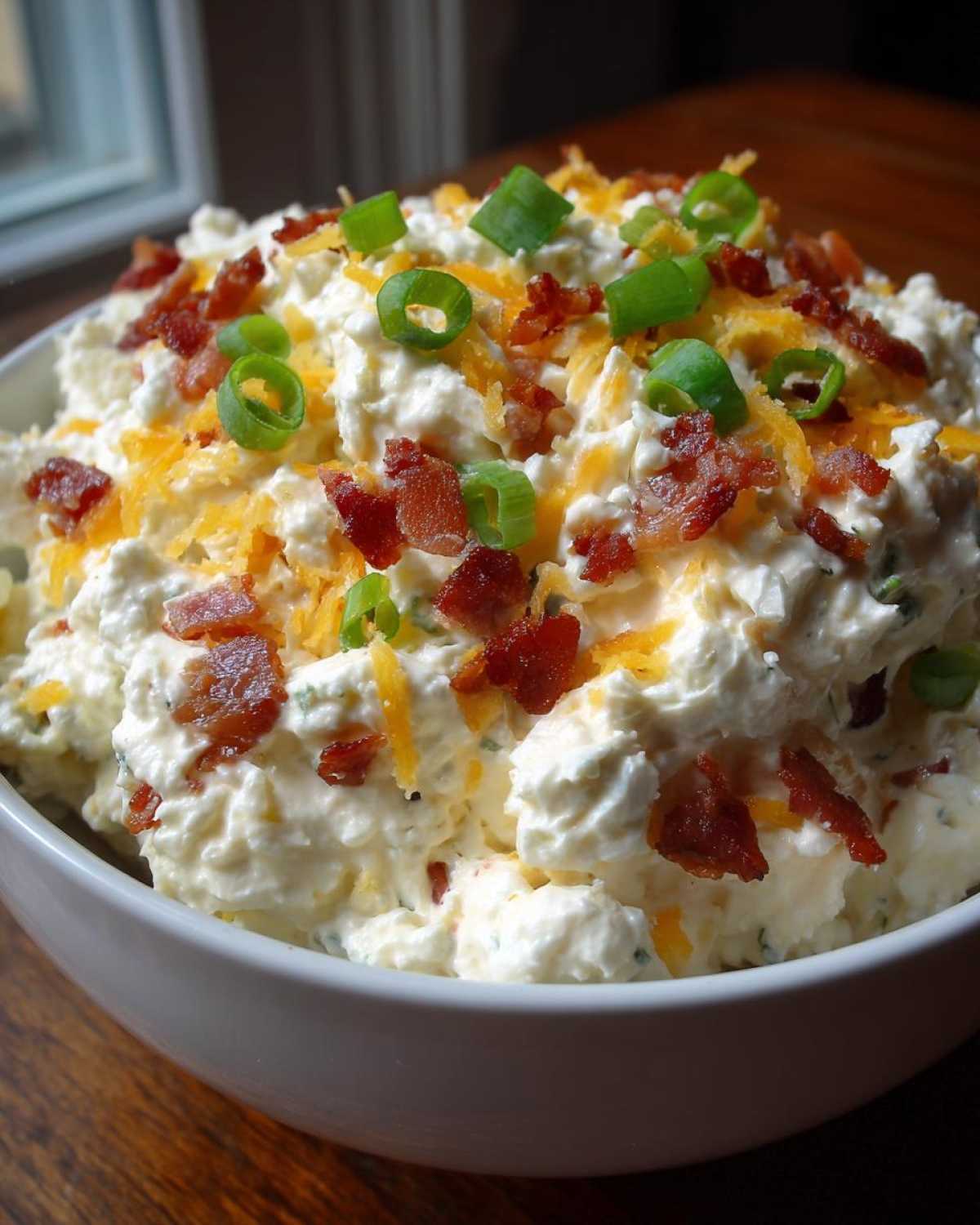 Close-up of a thick, creamy cream cheese dip topped generously with crumbled bacon, shredded cheddar cheese, and sliced green onions.