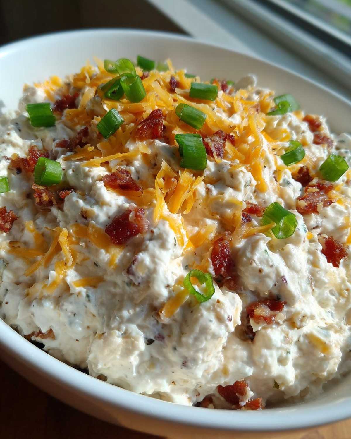 Close-up of a thick, creamy bacon ranch cream cheese dip topped with shredded cheddar and green onions.