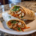 A cross-section view of a thai peanut chicken wrap filled with chicken, carrots, cabbage, and cilantro, drizzled with peanut sauce.