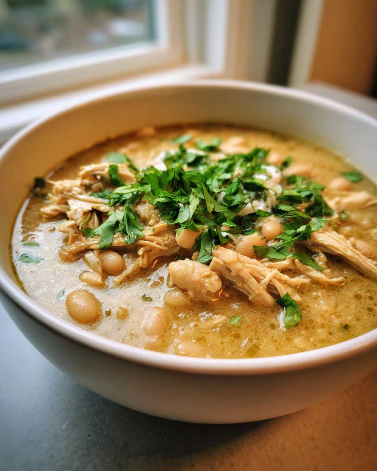 Close-up of a comforting bowl of white bean chicken chili, featuring shredded chicken and topped generously with fresh chopped cilantro.