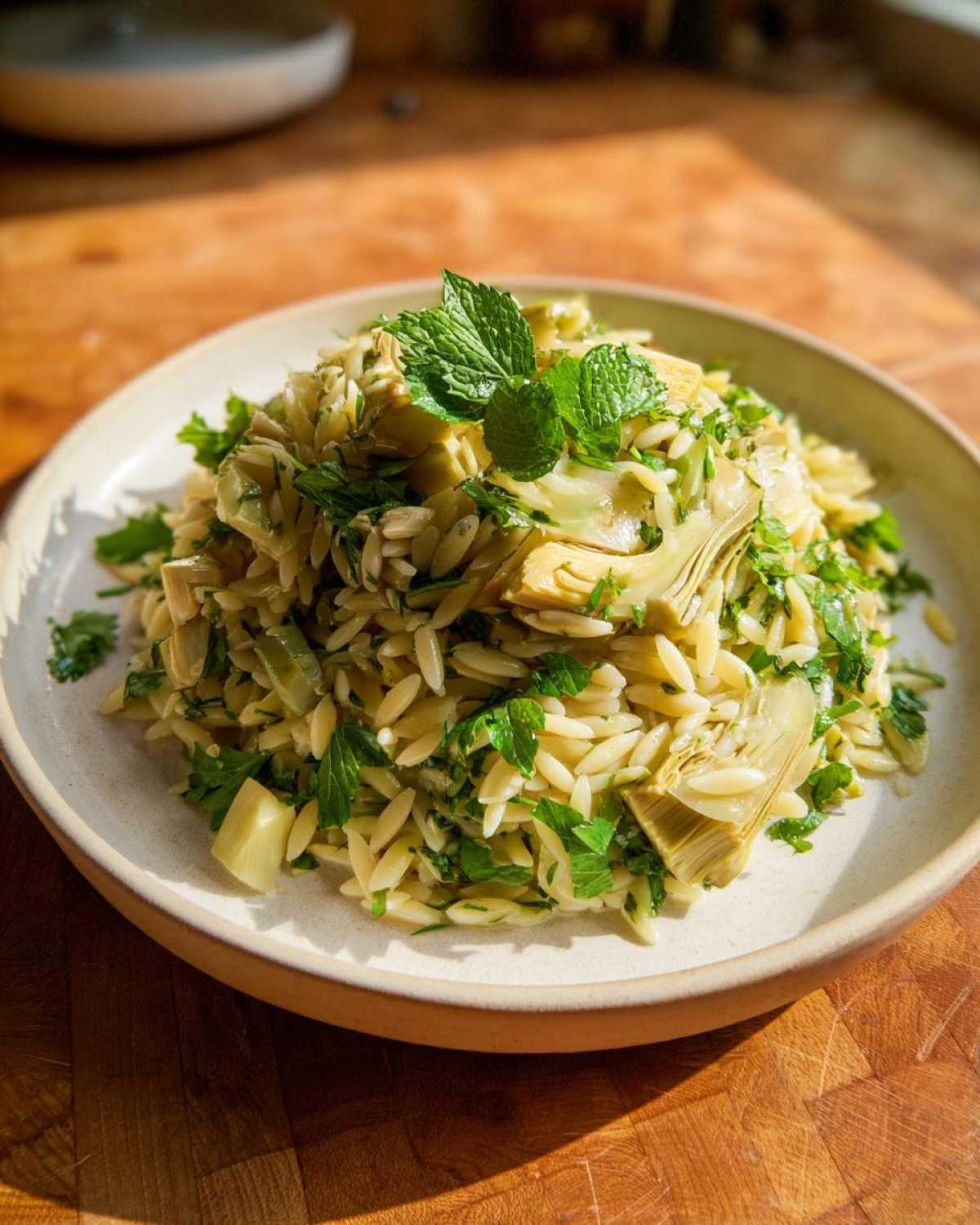 A serving of Artichoke Lemon Orzo Salad topped with fresh mint leaves on a light-colored plate.